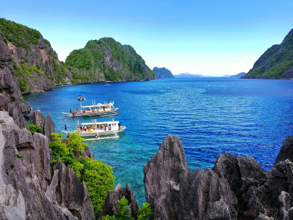 A breathtaking view of El Nido, Palawan, with clear blue waters, limestone cliffs, and tour boats anchored near the shore.