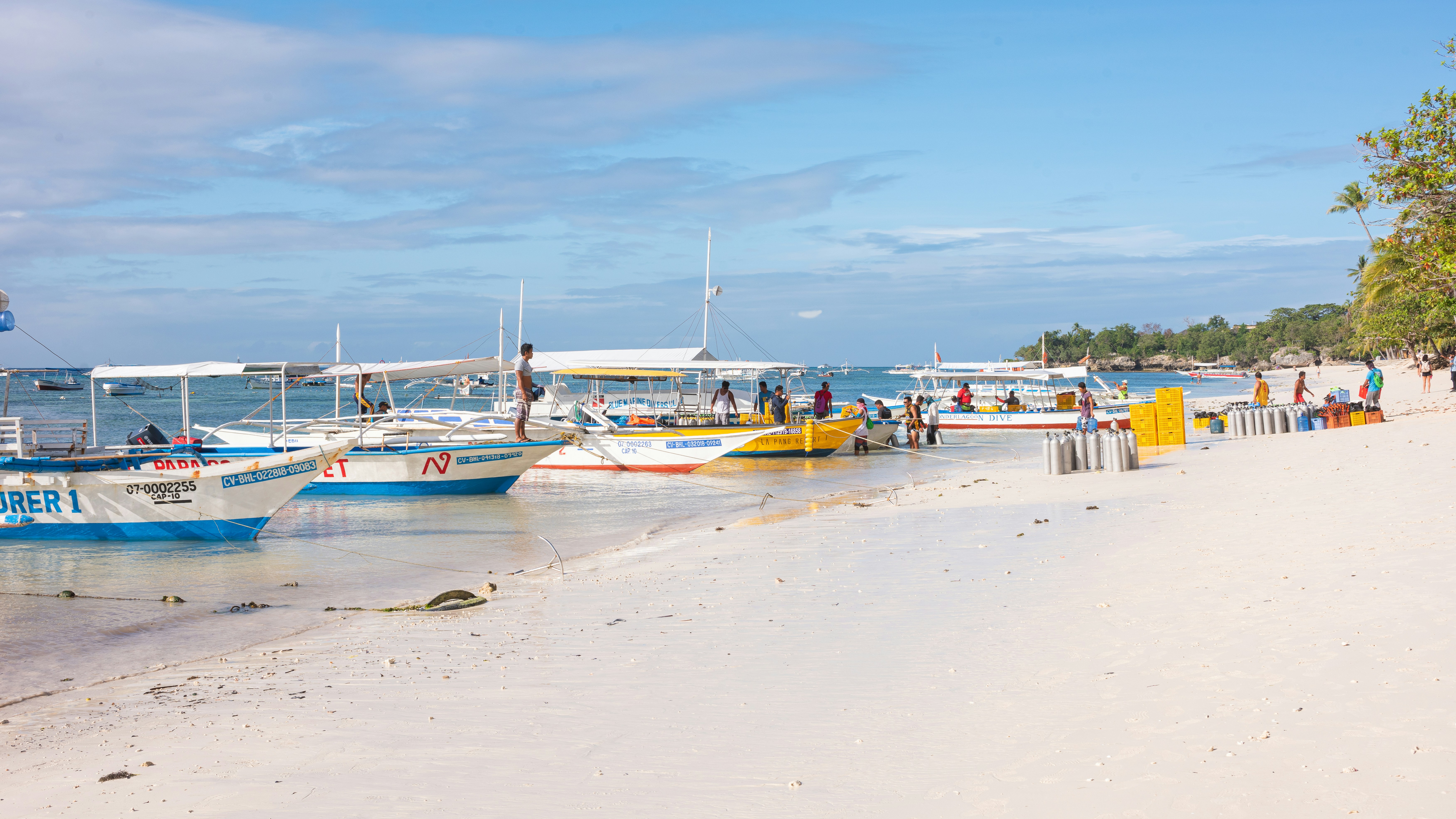 People preparing boats along the shoreline of Alona Beach, Panglao, with the clear blue ocean in the background.