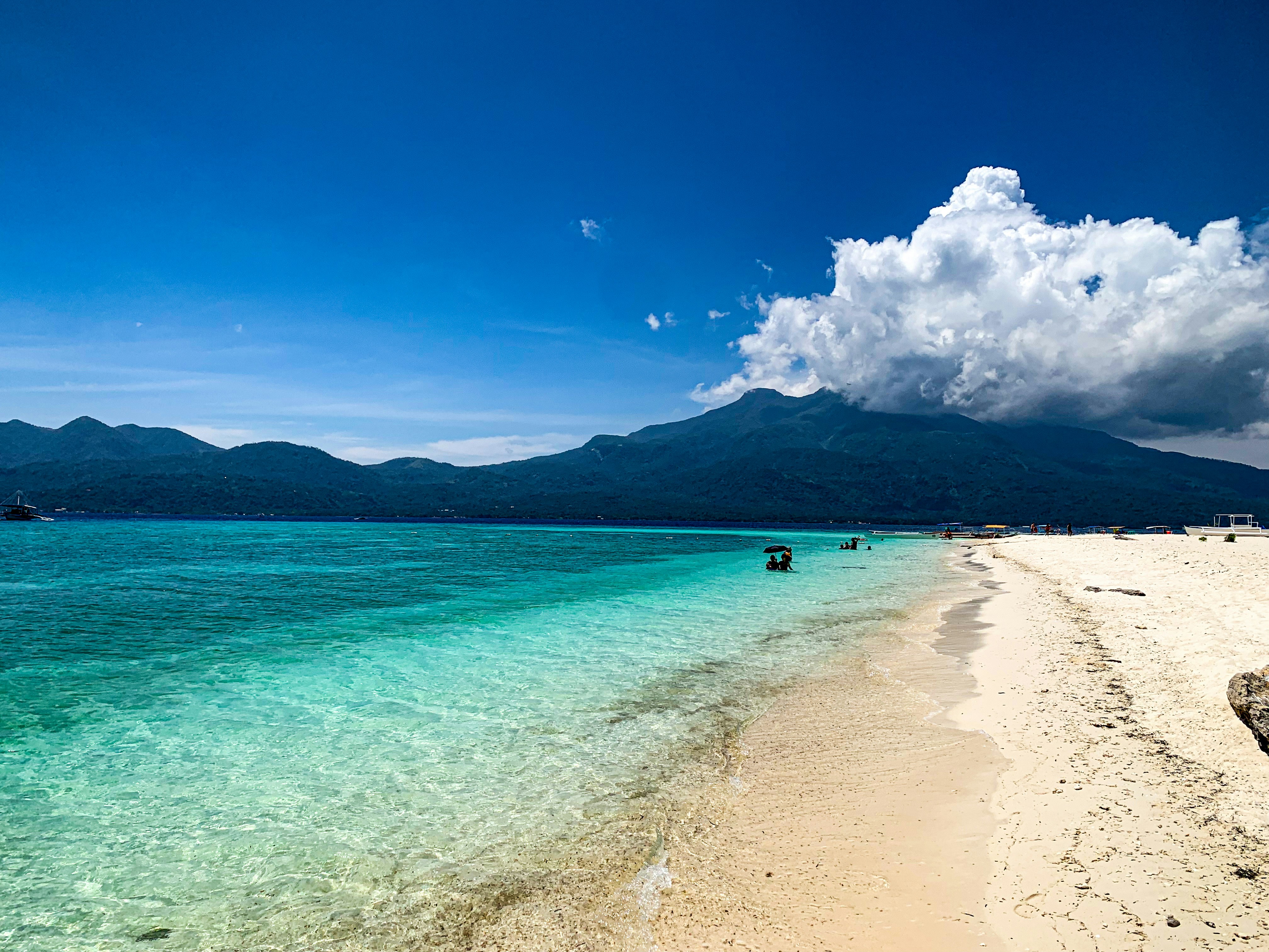 A pristine beach with crystal-clear turquoise waters and a mountainous backdrop under a bright blue sky in Camiguin, Philippines.