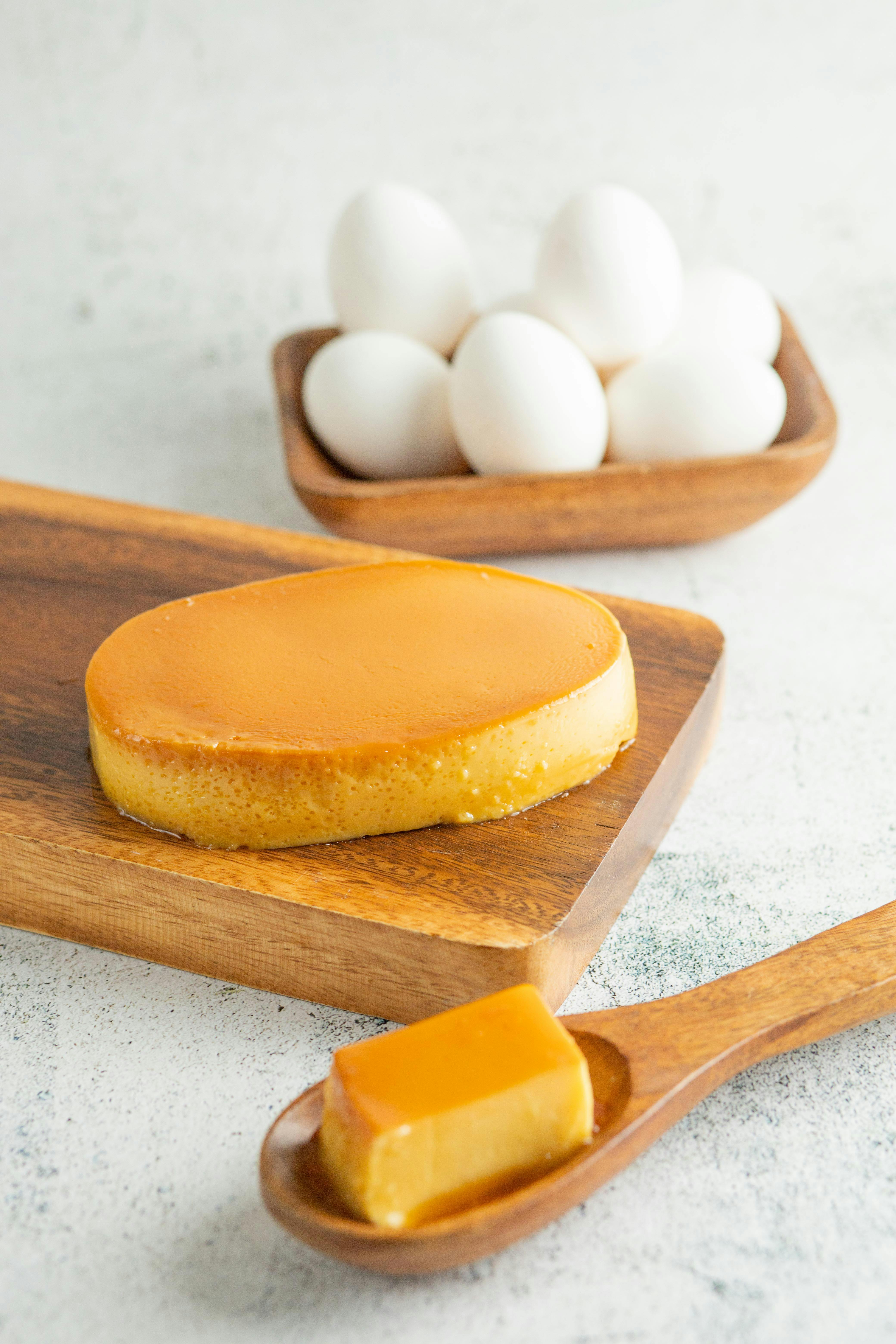 A creamy Filipino dessert leche flan rests on a wooden board accompanied by a bowl of fresh eggs in the background.