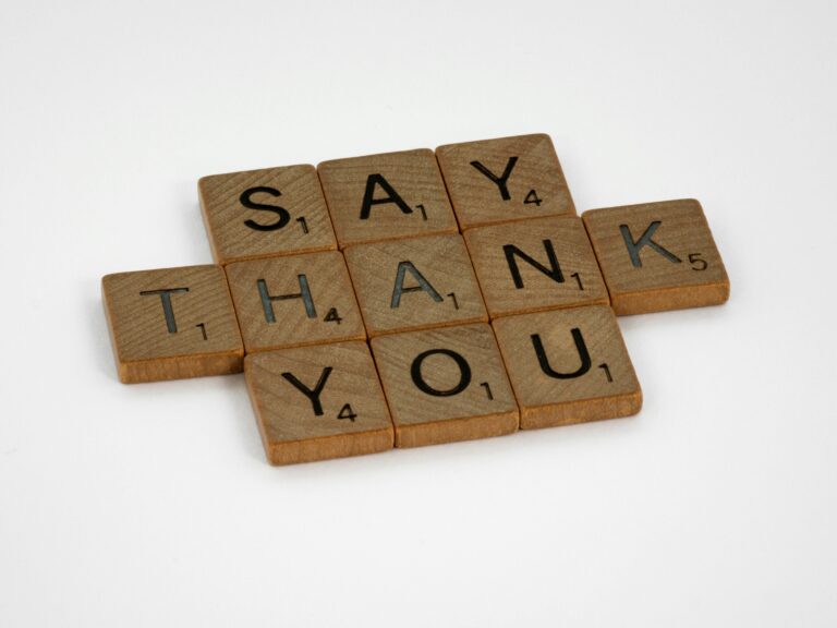 The image shows Scrabble tiles arranged to spell "SAY THANK YOU" on a white background.