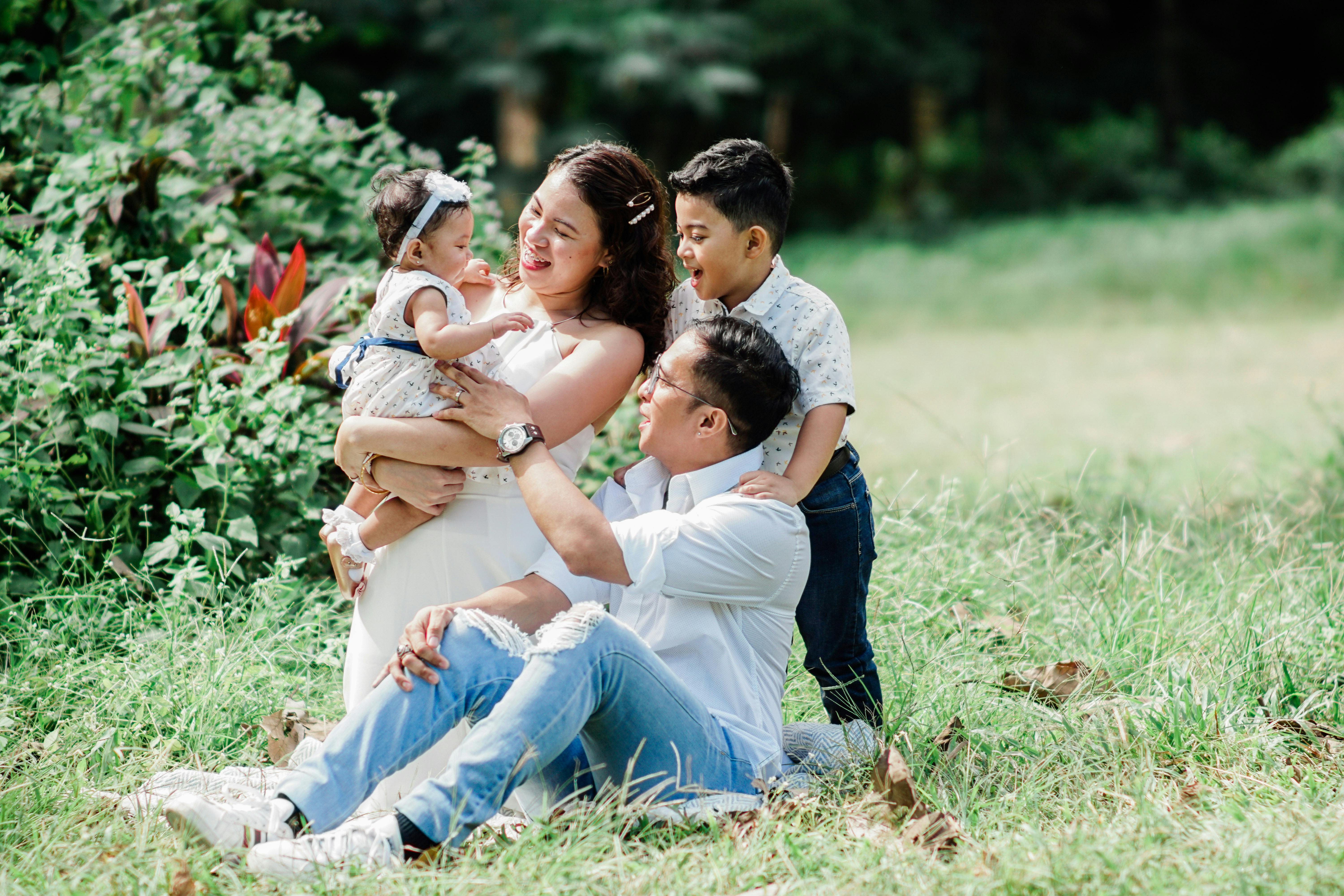 A Filipino family enjoys a moment together outdoors, sitting in a grassy area with the parents smiling at their two young children.