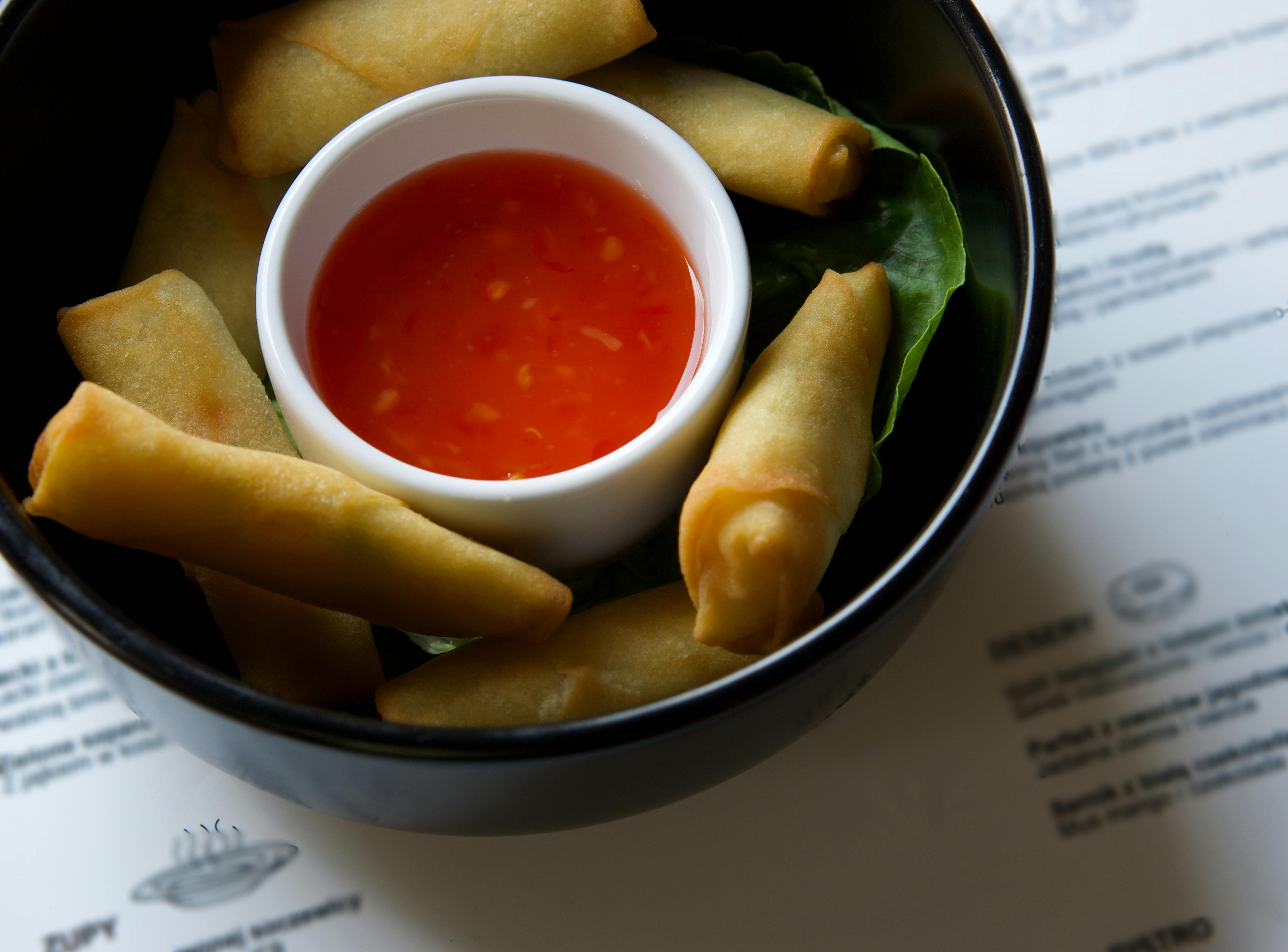 A bowl of golden, crispy Lumpiang Shanghai (Filipino spring rolls) is served with a side of sweet chili dipping sauce.