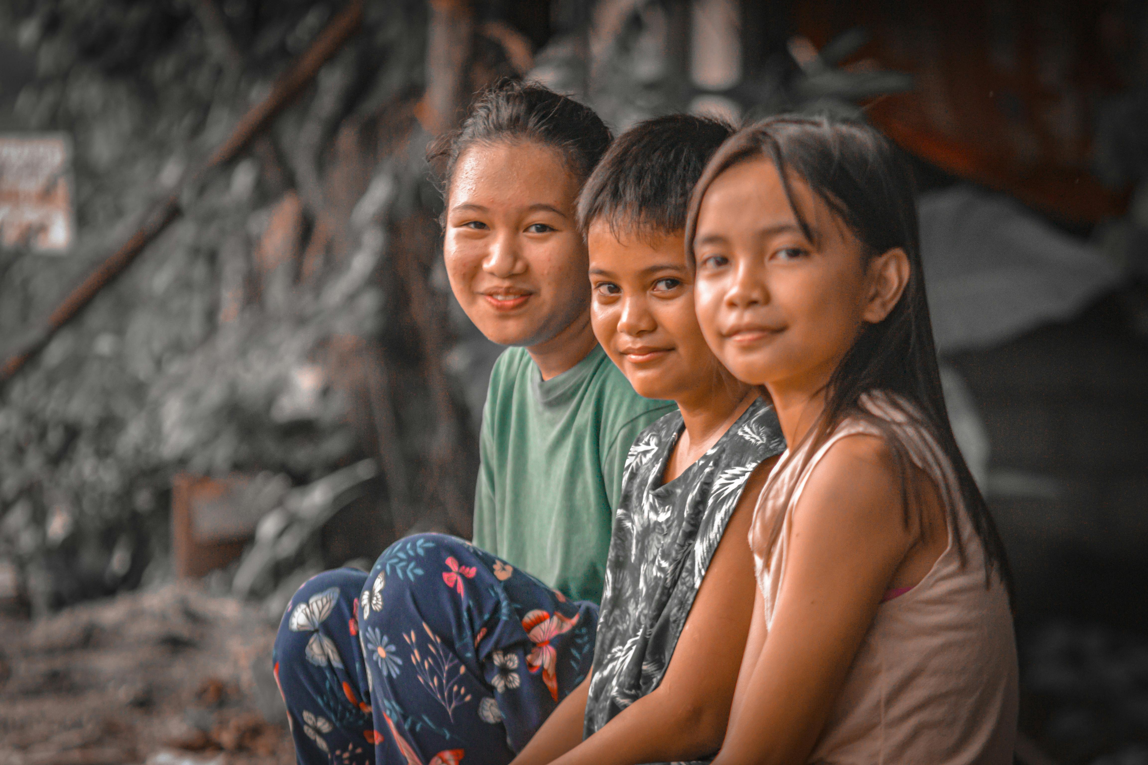 Three children smiling warmly while sitting close together, showcasing their bond and happiness.