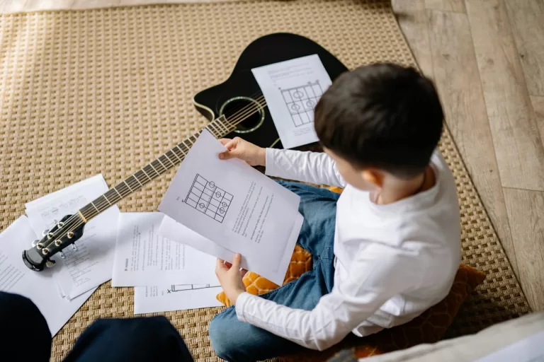 A boy holding a paper with a guitar beside him